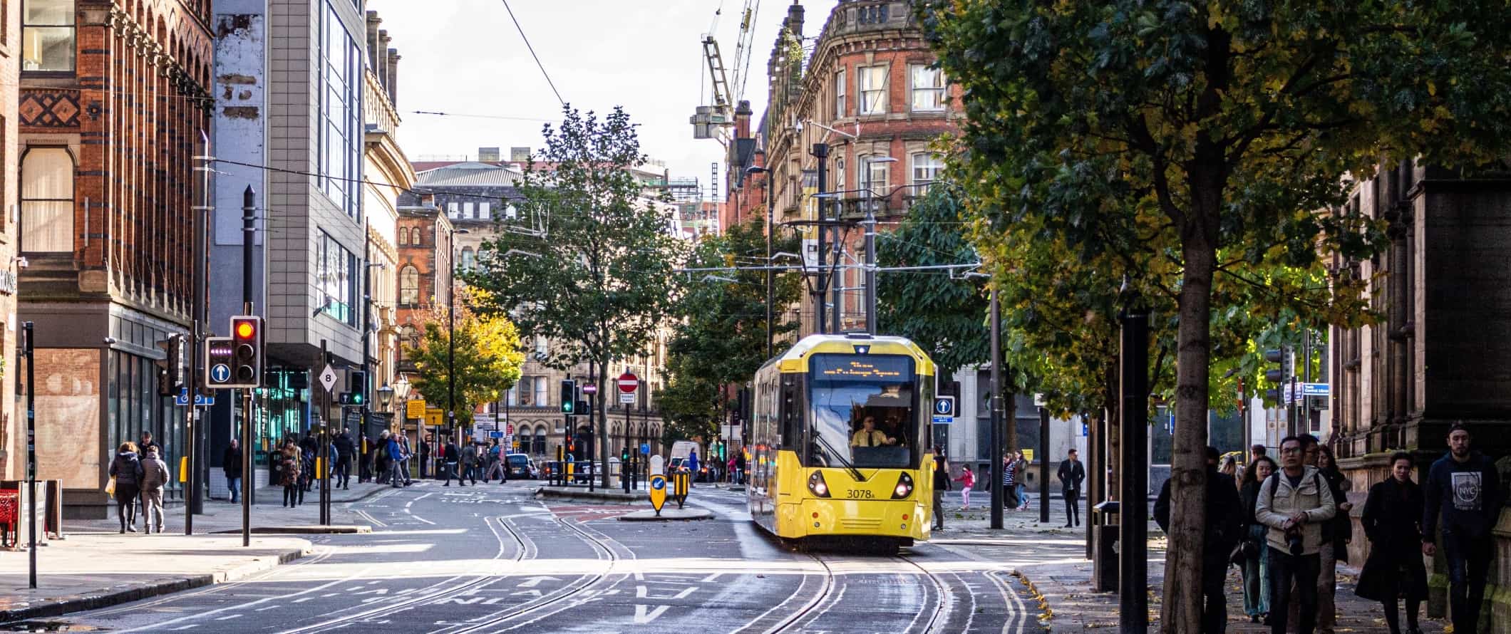 Street view of people walking down the street and a yellow tram passing by in Manchester, England