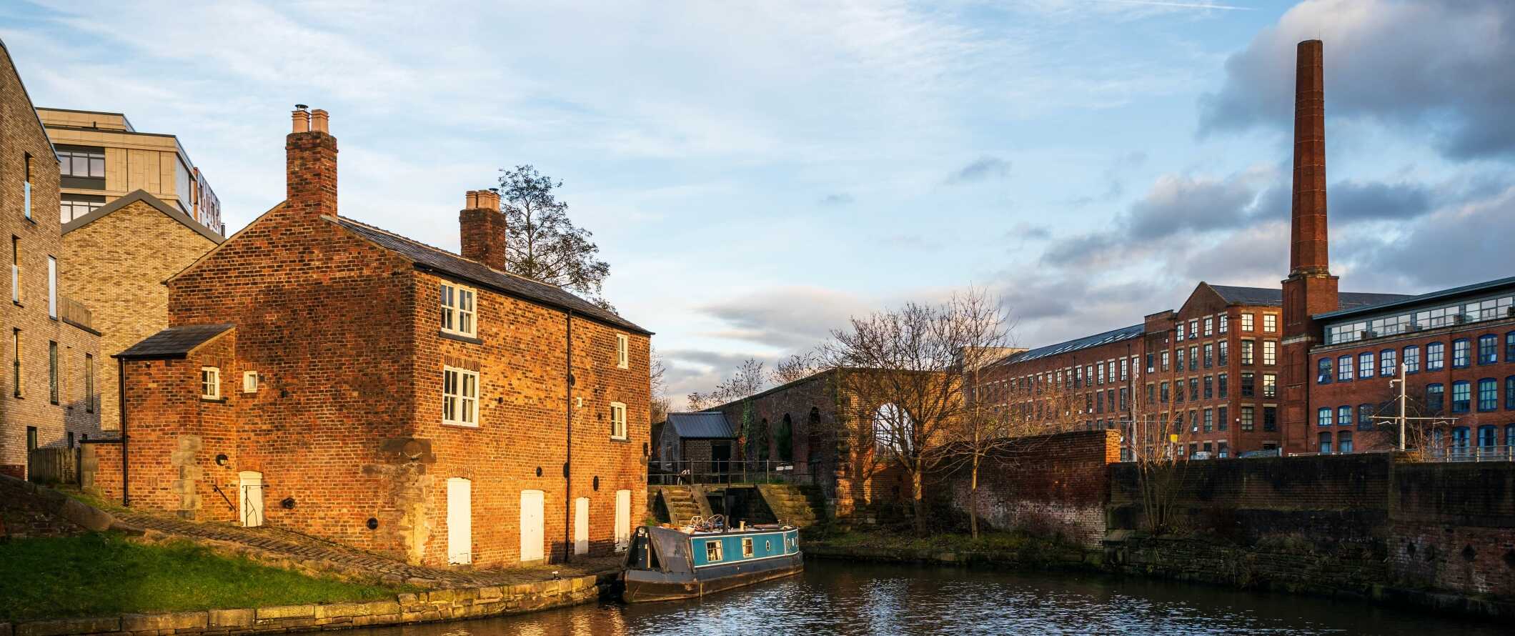 Historic brick buildings and a warehouse along a canal with a small boat in it in Manchester, England