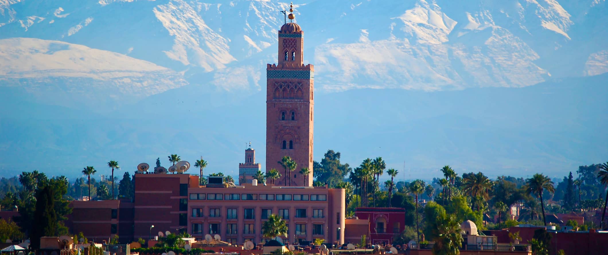 city view of Marrakesh, Morocco featuring a tower in the foreground and stunning mountains in the distance