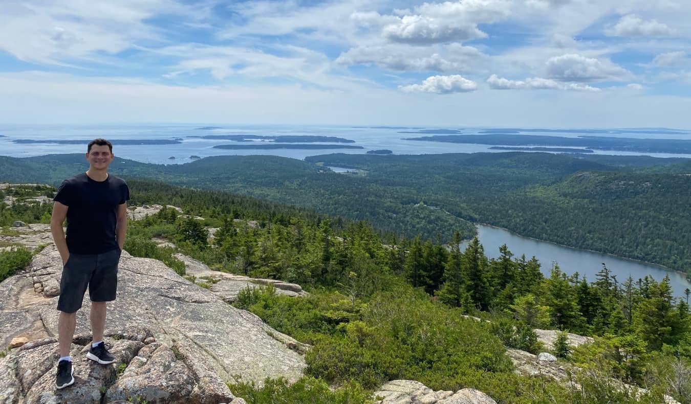 Matt standing on top of a mountain with a lush archipelago behind him in Maine, USA