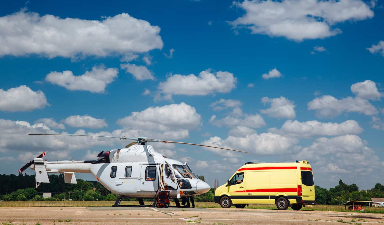 A helicopter parked in a lot with a small ambulance during an emergency