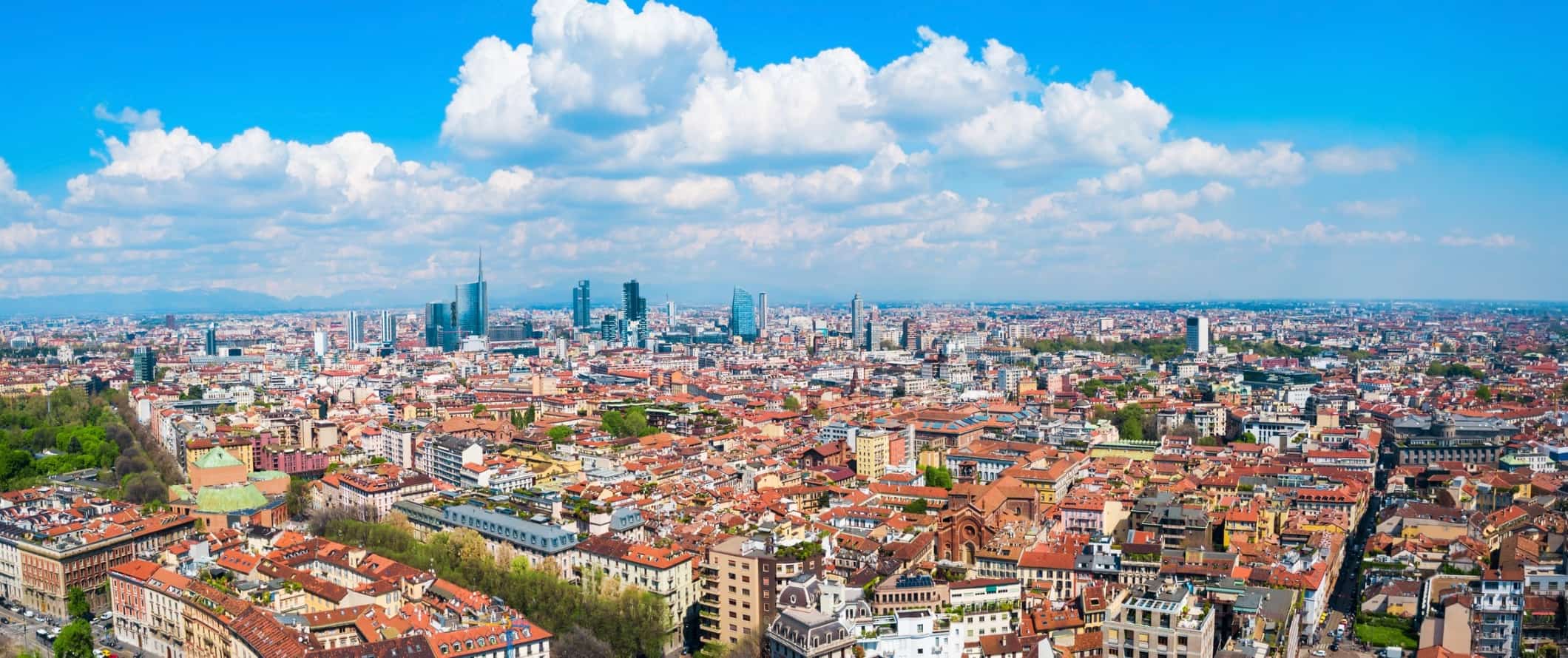 The gorgeous and sprawling city skyline of Milan, Italy on a sunny day with mountains in the background