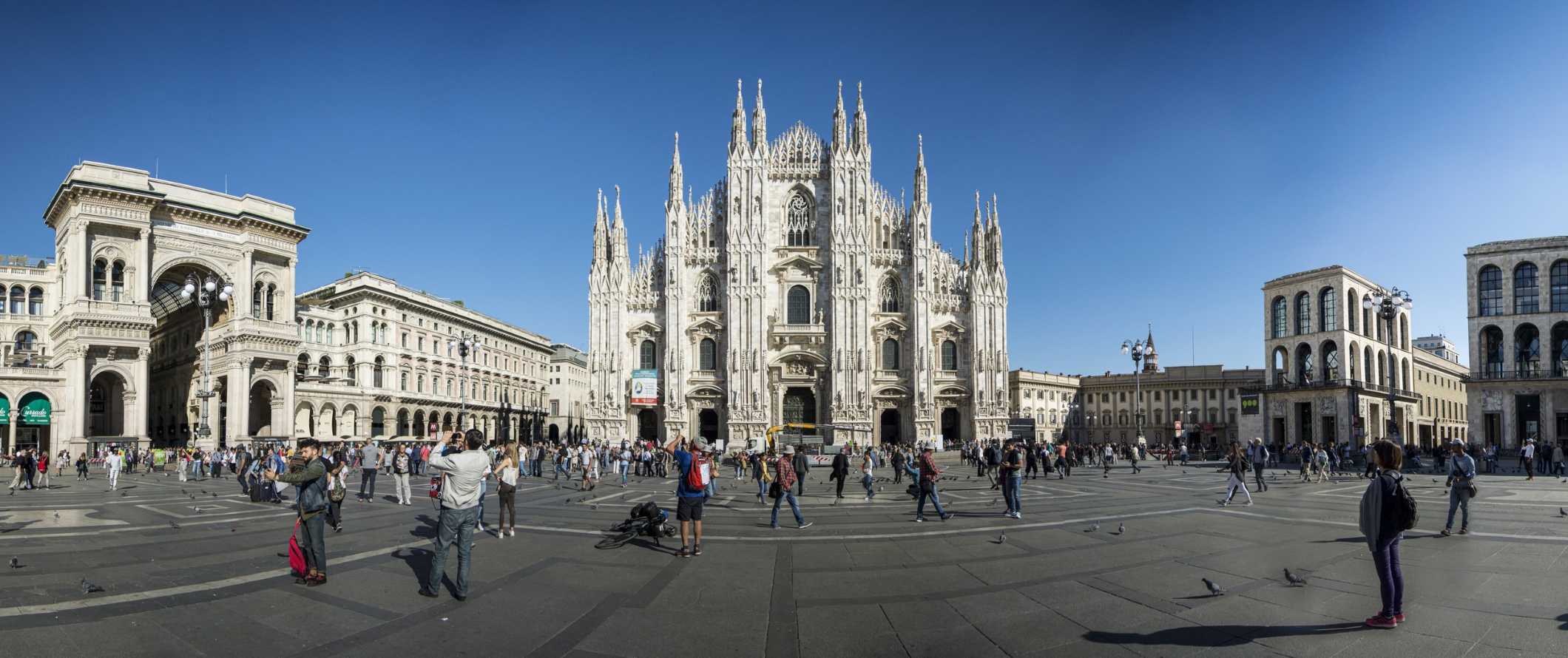 Panoramic view of Milan's cathedral and plaza in front with people standing around taking photos.
