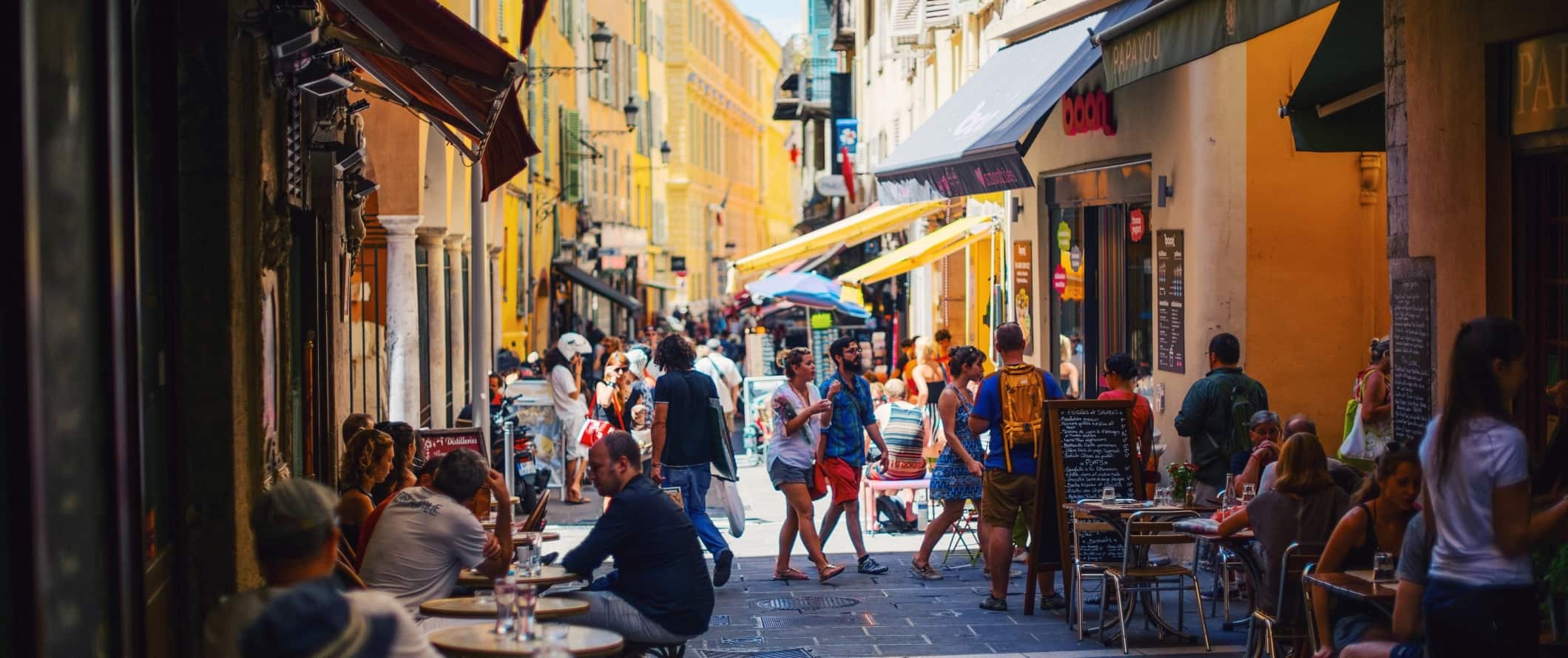 A busy pedestrian street filled with people walking around and sitting down at outdoor cafes in the old town in Nice, France