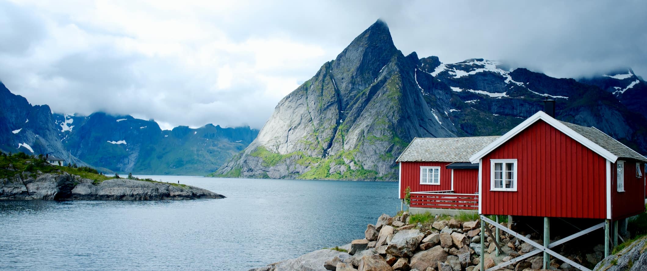 scenic fjords in Norway with a red cabin in the foreground along the rugged coastline