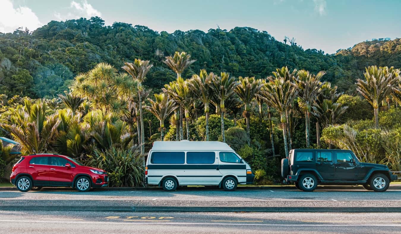 A car, campervan, and Jeep on the road in the rainforests of New Zealand.