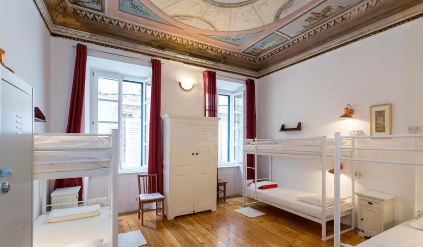 Dorm room with bunk beds, wood floors, and an ornate ceiling at Old Town Hostel in Dubrovnik, Croatia.