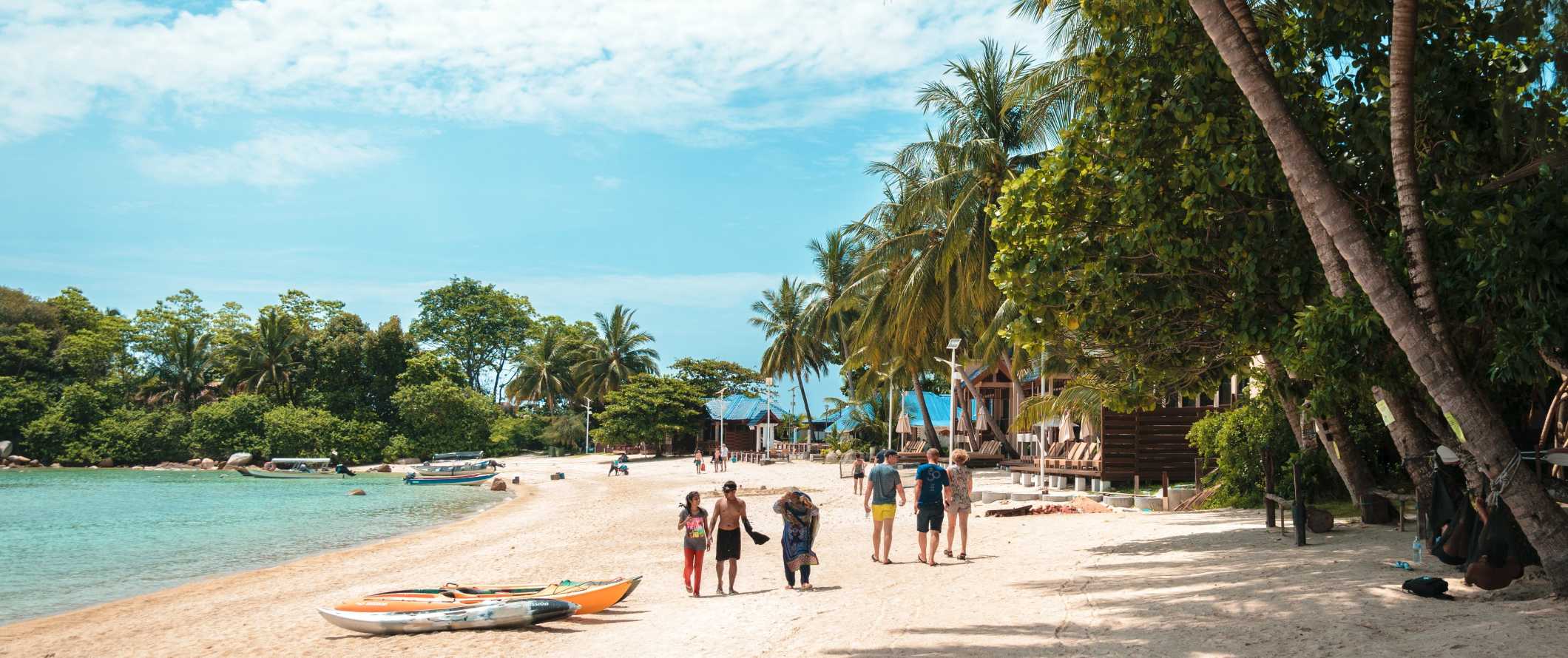 People walking down the beach with clear waters and lush palm trees in Perhentian Islands, Malaysia