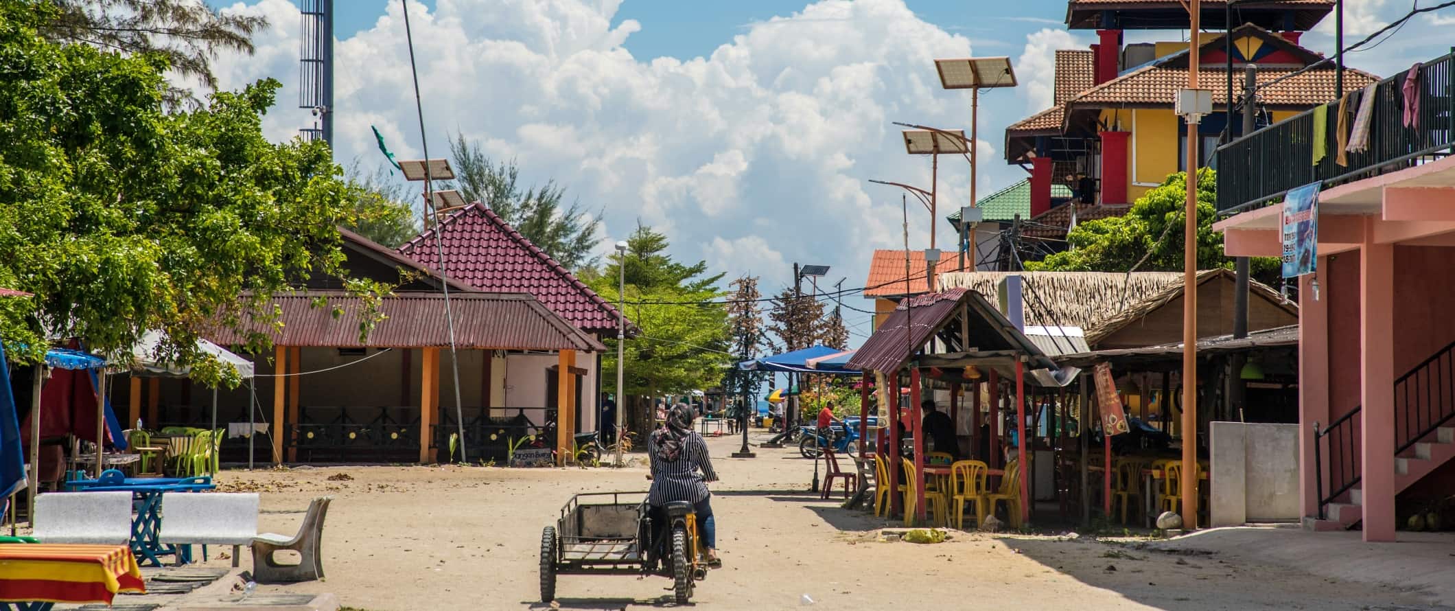A person riding a motorbike down a sandy street with low buildings on both sides in the Perhentian Islands, Malaysia