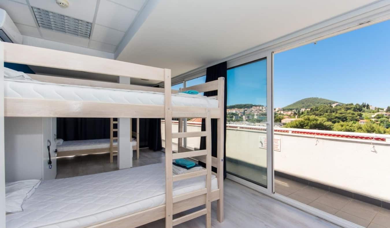 Bunk beds with sliding glass doors opening to balcony overlooking lush hills at Hostel Petra Marina in Dubrovnik, Croatia.