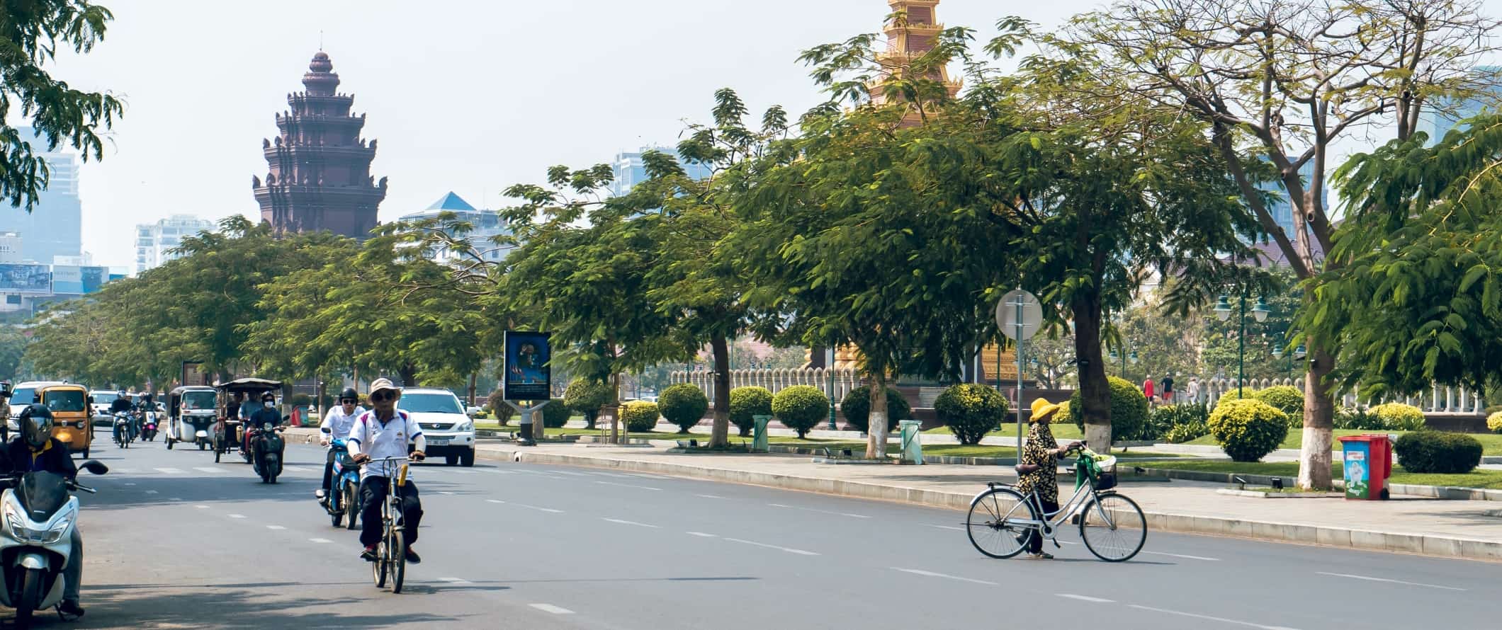 People biking and motorbiking down a wide street in Phnom Penh, Cambodia