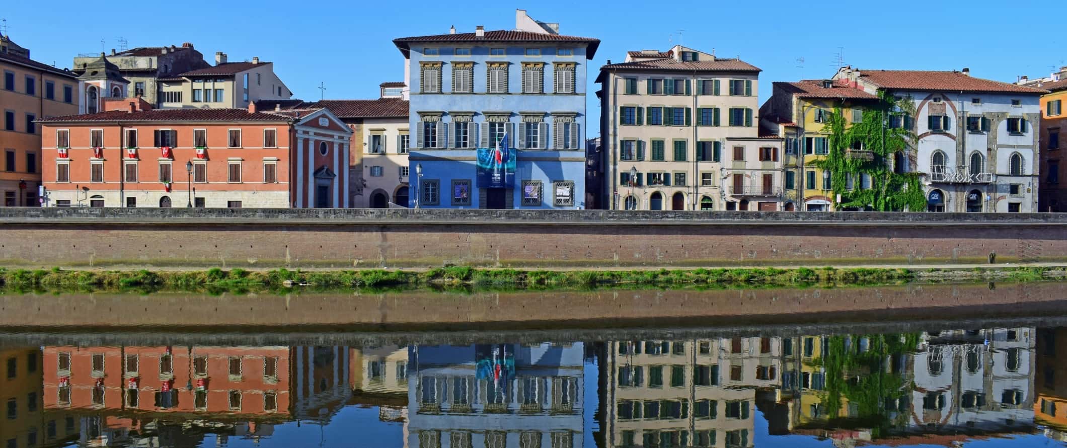 Brightly colored historic buildings, including the blue-colored art center, Palazzo Blu, along the banks of the Arno River in Pisa, Italy.