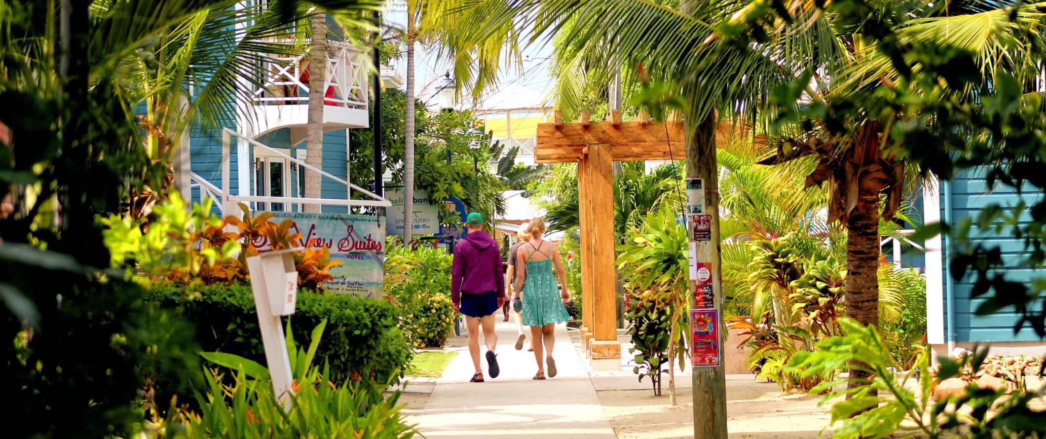 Tourists walking down a sidewalk lined with lush palms in Placencia, Belize