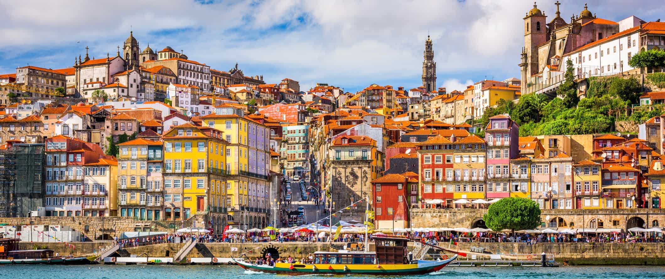 A boat passing by the colorful coast of Porto, Portugal on a busy summer day