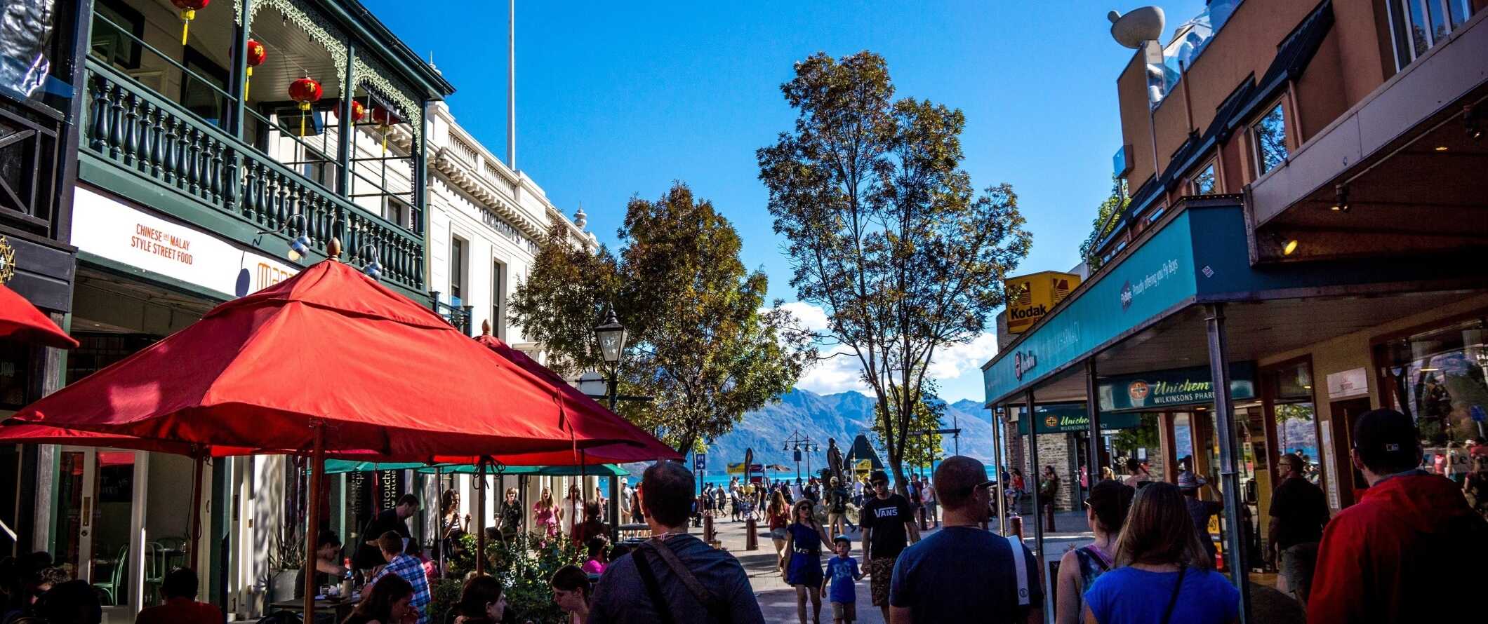 People walking down the street of historic Queenstown, New Zealand, with the lake and mountains in the background