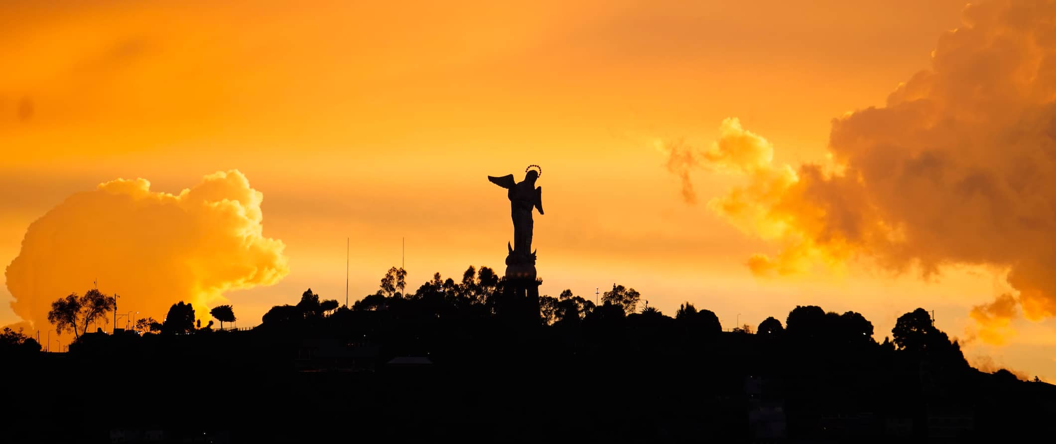 A statue on a hill silhouetted during a brilliant orange sunset