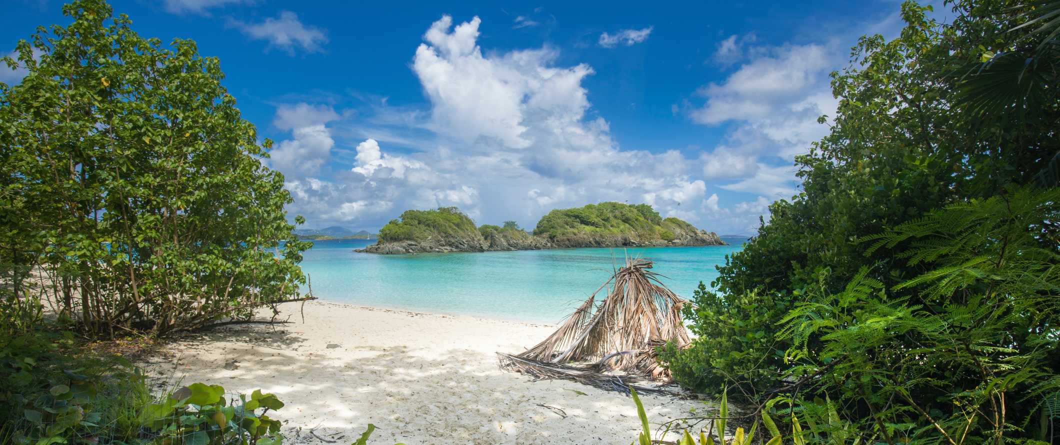 View of a white sand beach and small island in the distance on the island of Saint John, USVI