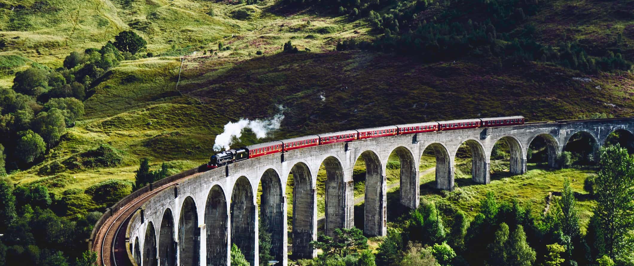 The famous steam train from Harry Potter crossing an old bridge in Scotland
