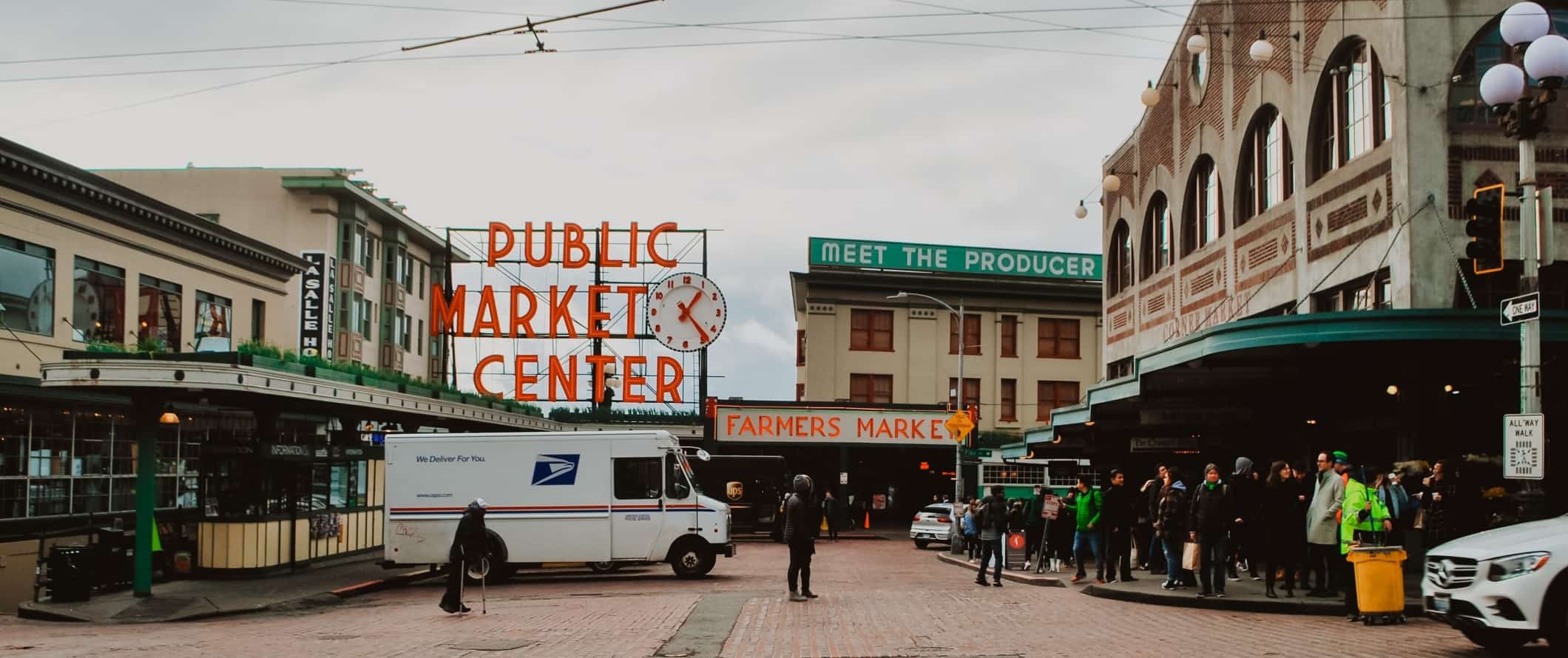 Neon sign saying 'Public Market Center' with people clustered around historic market buildings in Seattle, Washington.