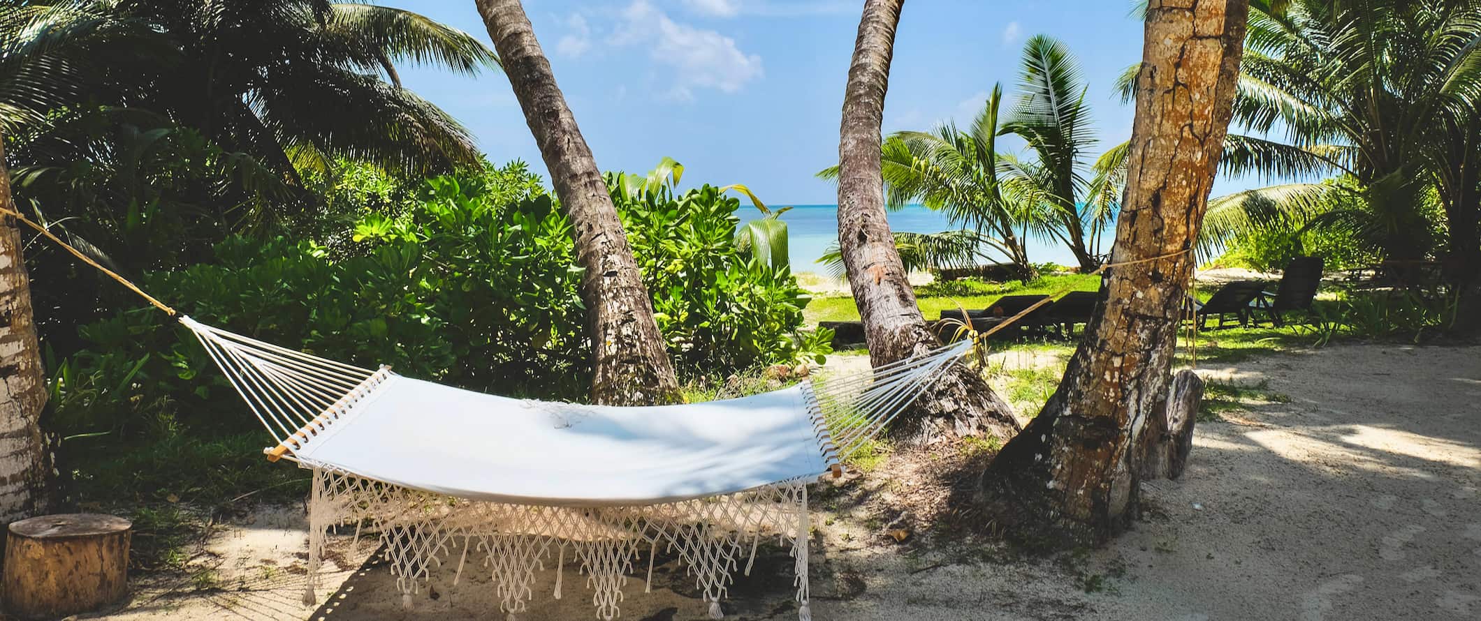 A tropical beach with a hammock set up in Seychelles with white sand and a bright blue sky above
