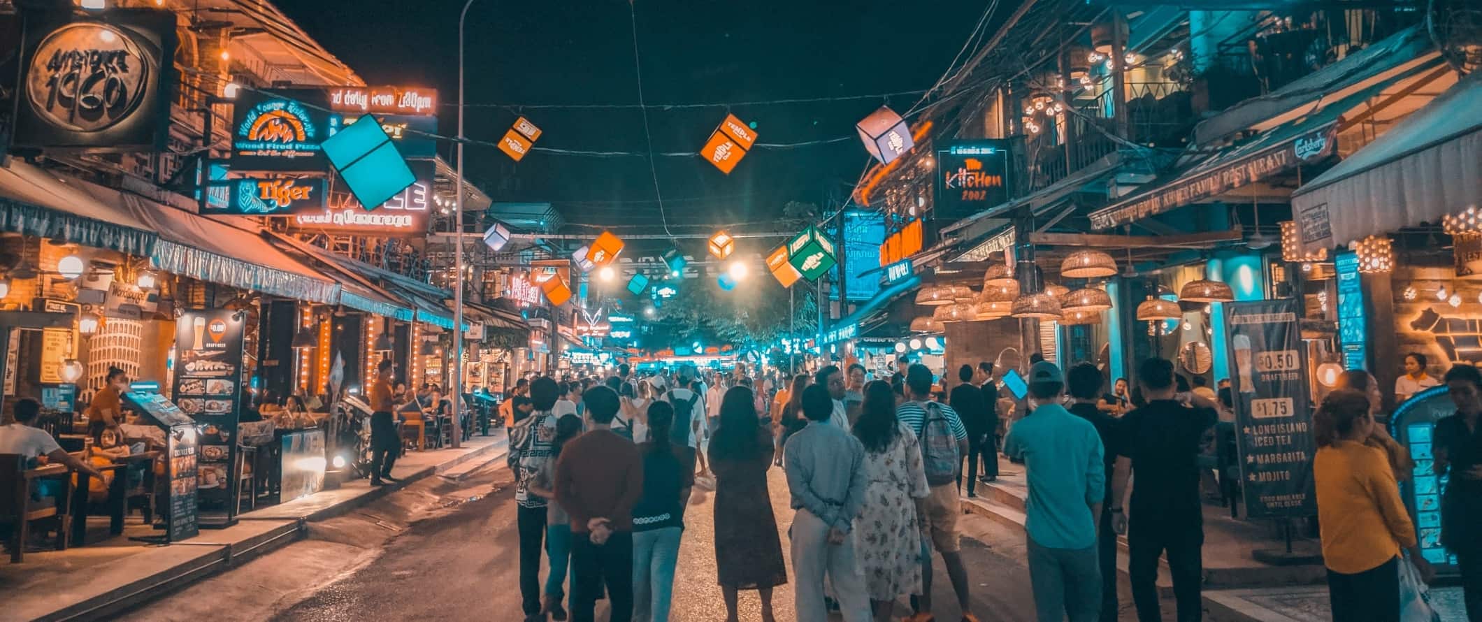 People walking down a street lined with food stalls all lit up at night in Siem Reap, Cambodia