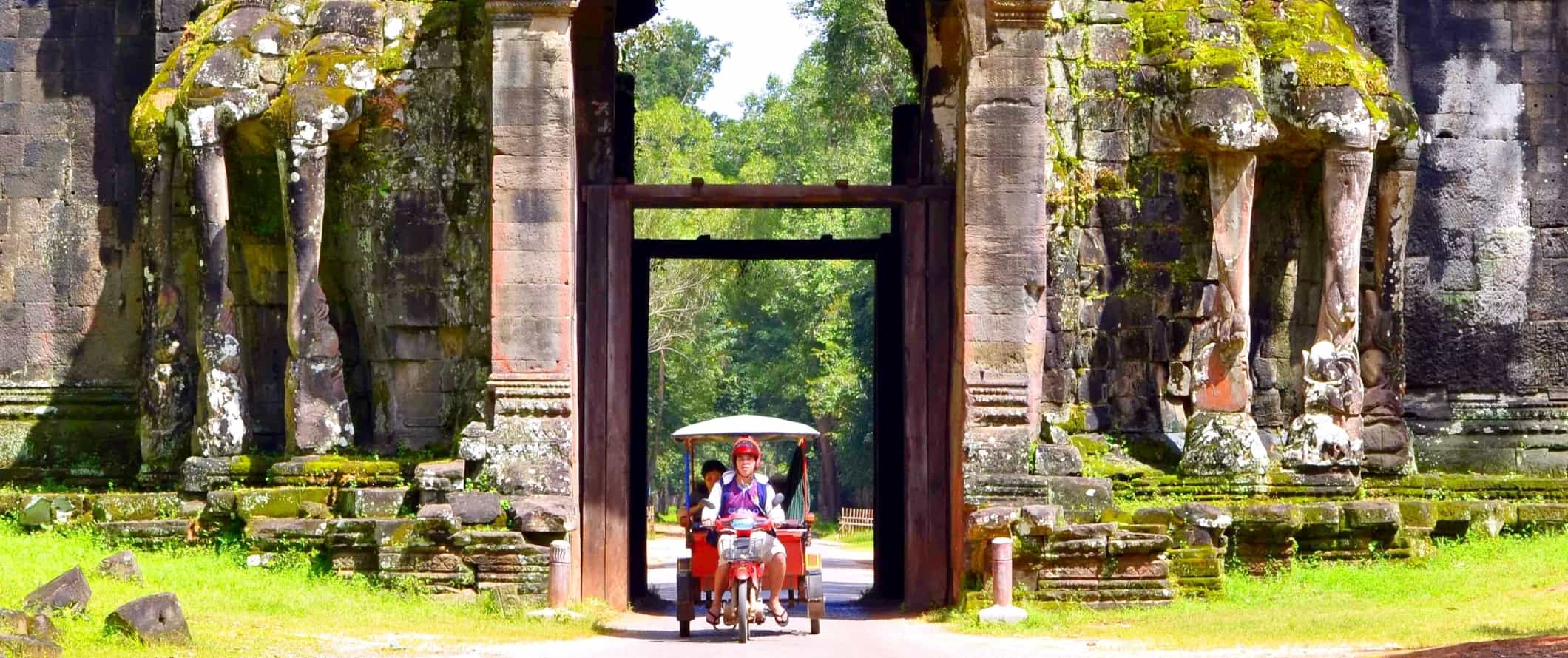 Tuk tuk passing through a large, intricately carved entranceway in the historic temple complex of Angkor Wat in Cambodia