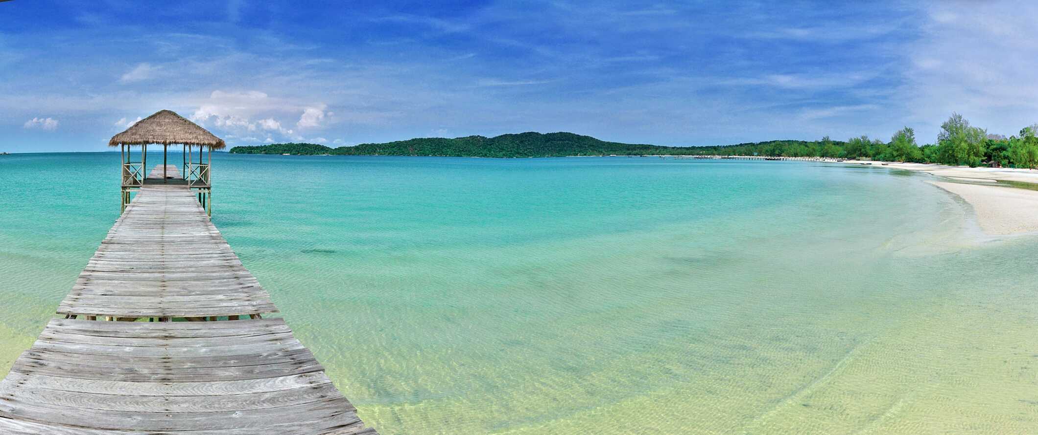 Thatched hut at the end of a wooden dock jutting into the clear turquoise water from the white sand beaches of Sihanoukville, Cambodia