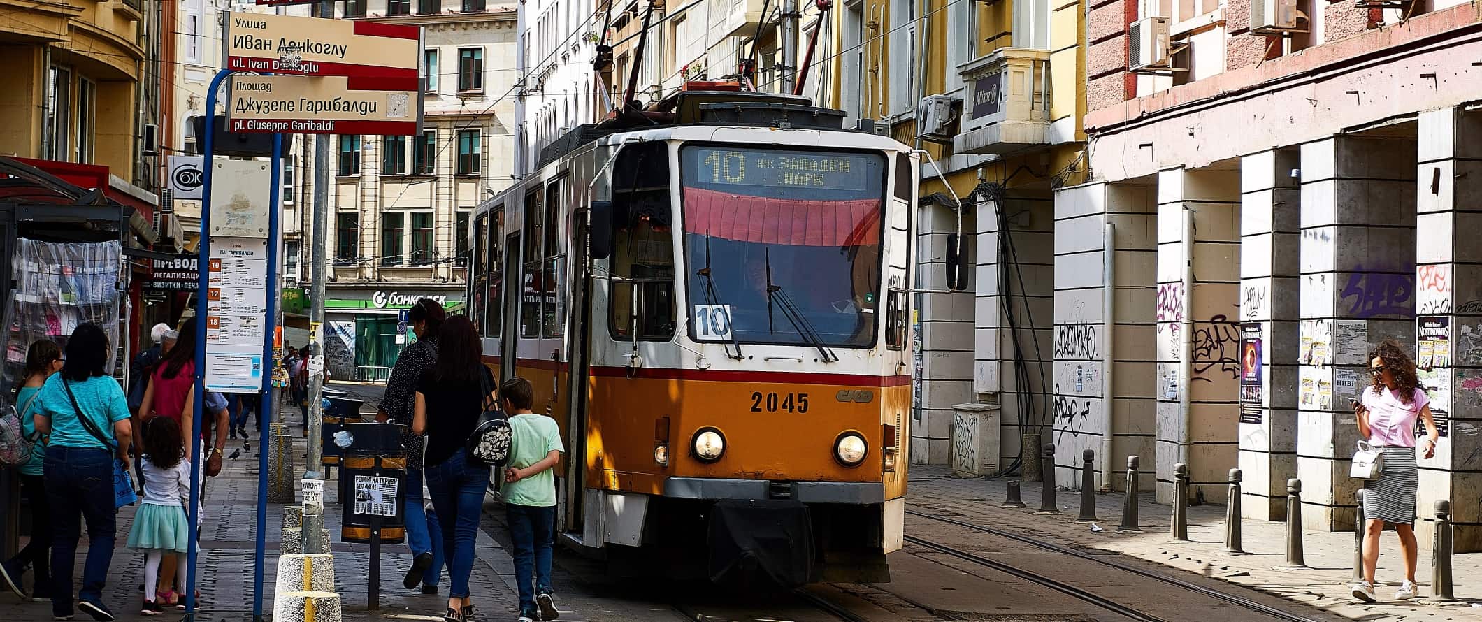 Yellow tram stopping in the middle of the street for people to get on in Sofia, Bulgaria