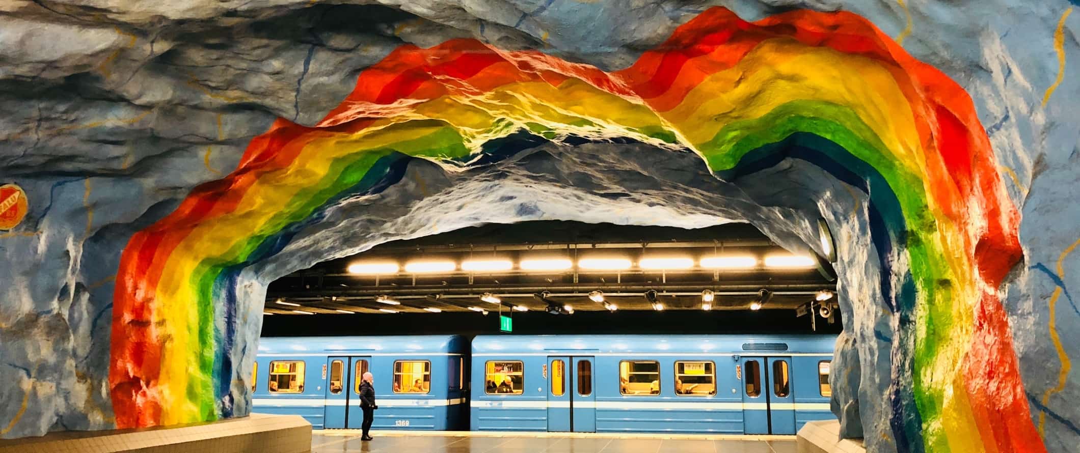 A rainbow mural in the subway with a blue train pulling into the station in Stockholm, Sweden