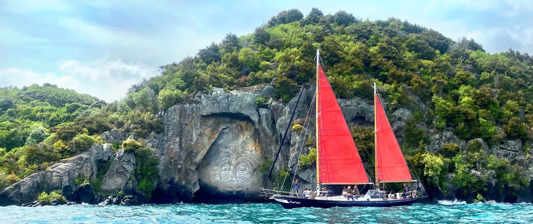 Sailboat passing by Maori rock carving on Lake Taupo in New Zealand.