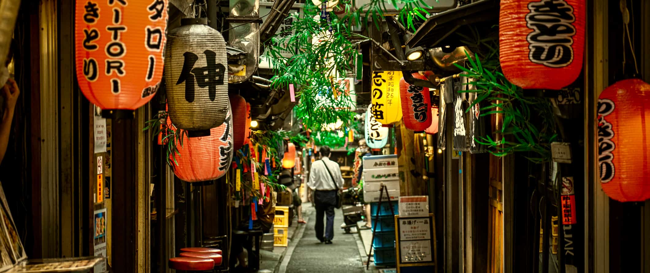 A man walking down a narrow alleyway lined by shops in Tokyo, Japan