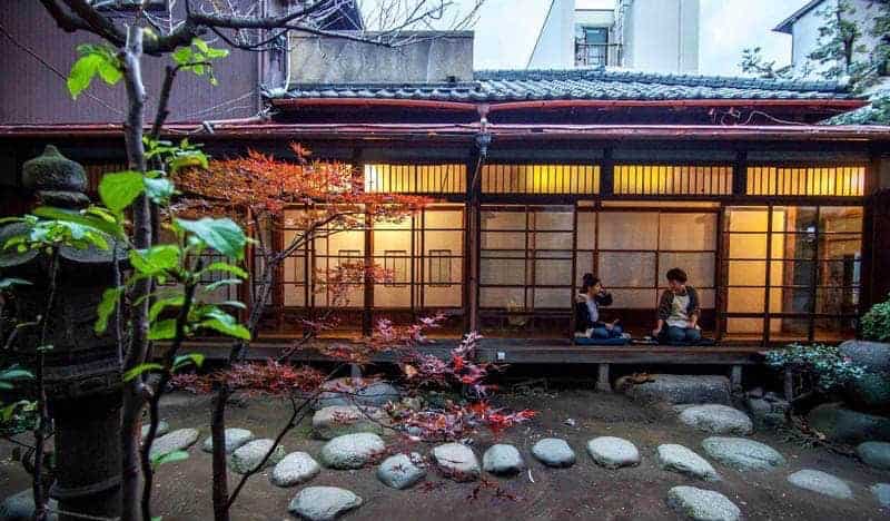 Interior courtyard with traditional Japanese garden and people sitting outside wooden screen doors of Toco Tokyo Hostel