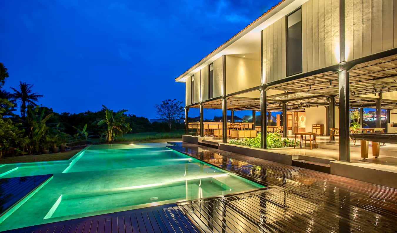 The exterior of Tribal Bali Hostel lit up at night with the pool in the foreground.