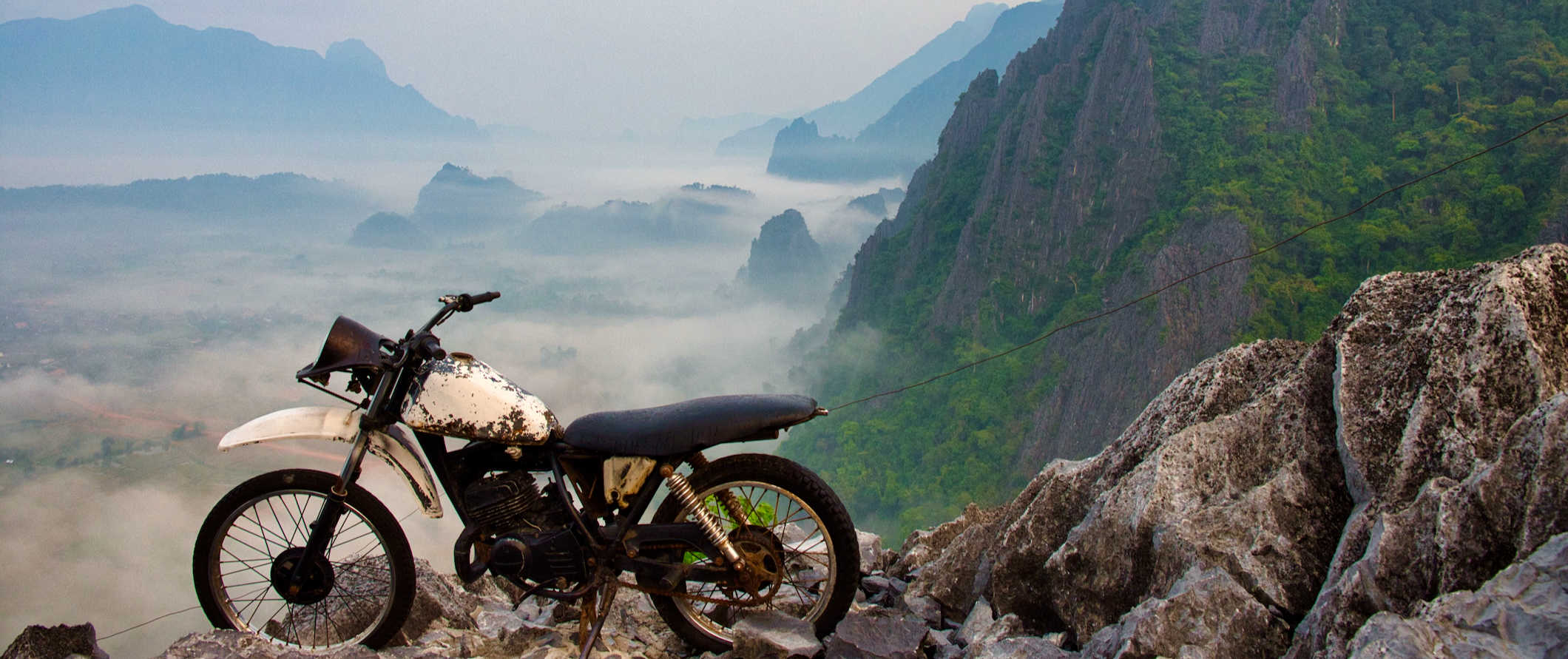 An old motorbike parked on a mountain overlooking the landscape near Vang Vieng, Laos