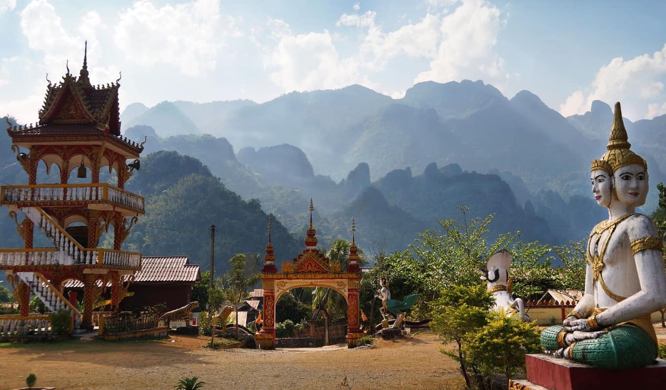 Buddhist statue, pagoda, and red gate against mountains in Vang Vieng, Laos