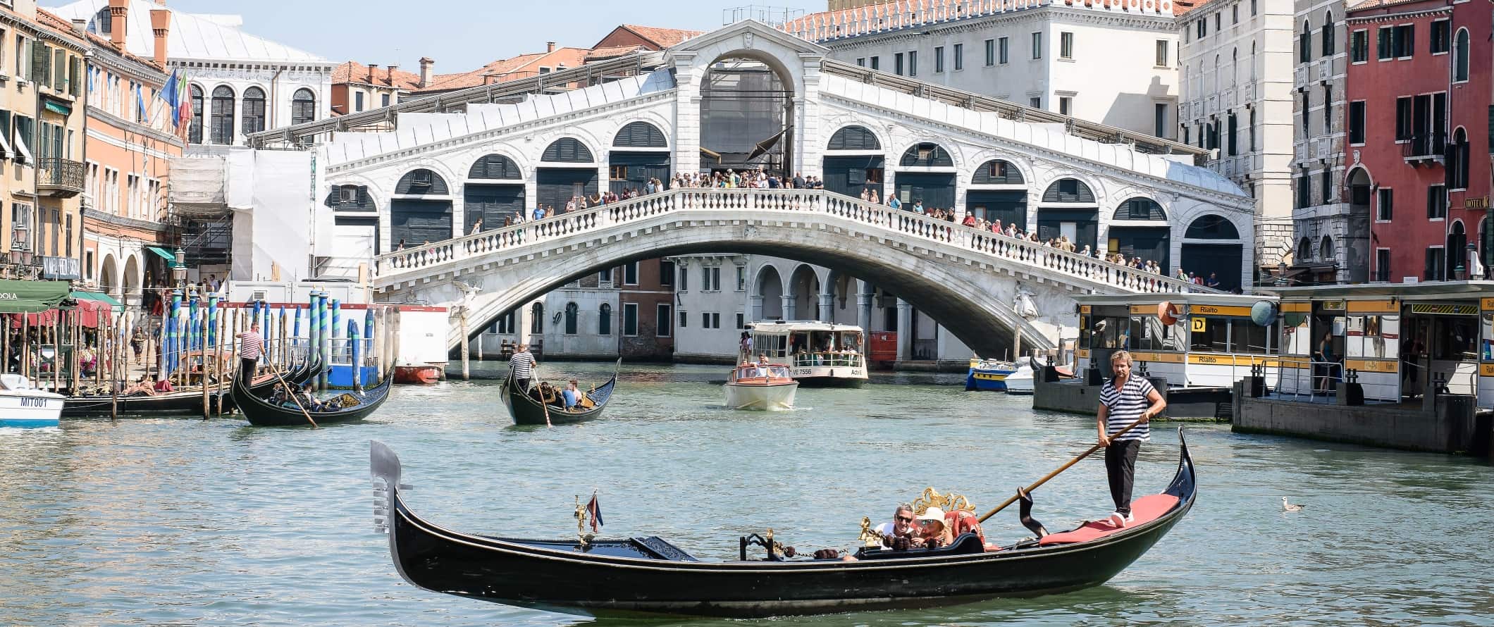 View of the historic Rialto bridge with a man steering a gondola in front, in Venice, Italy.