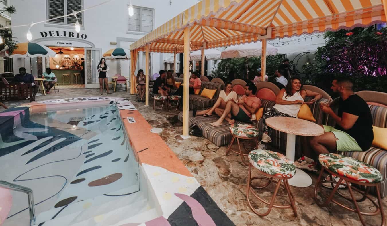 People sitting at small tables next to outdoor pool with colorful tiles at Viajero Hostel in Miami, Florida