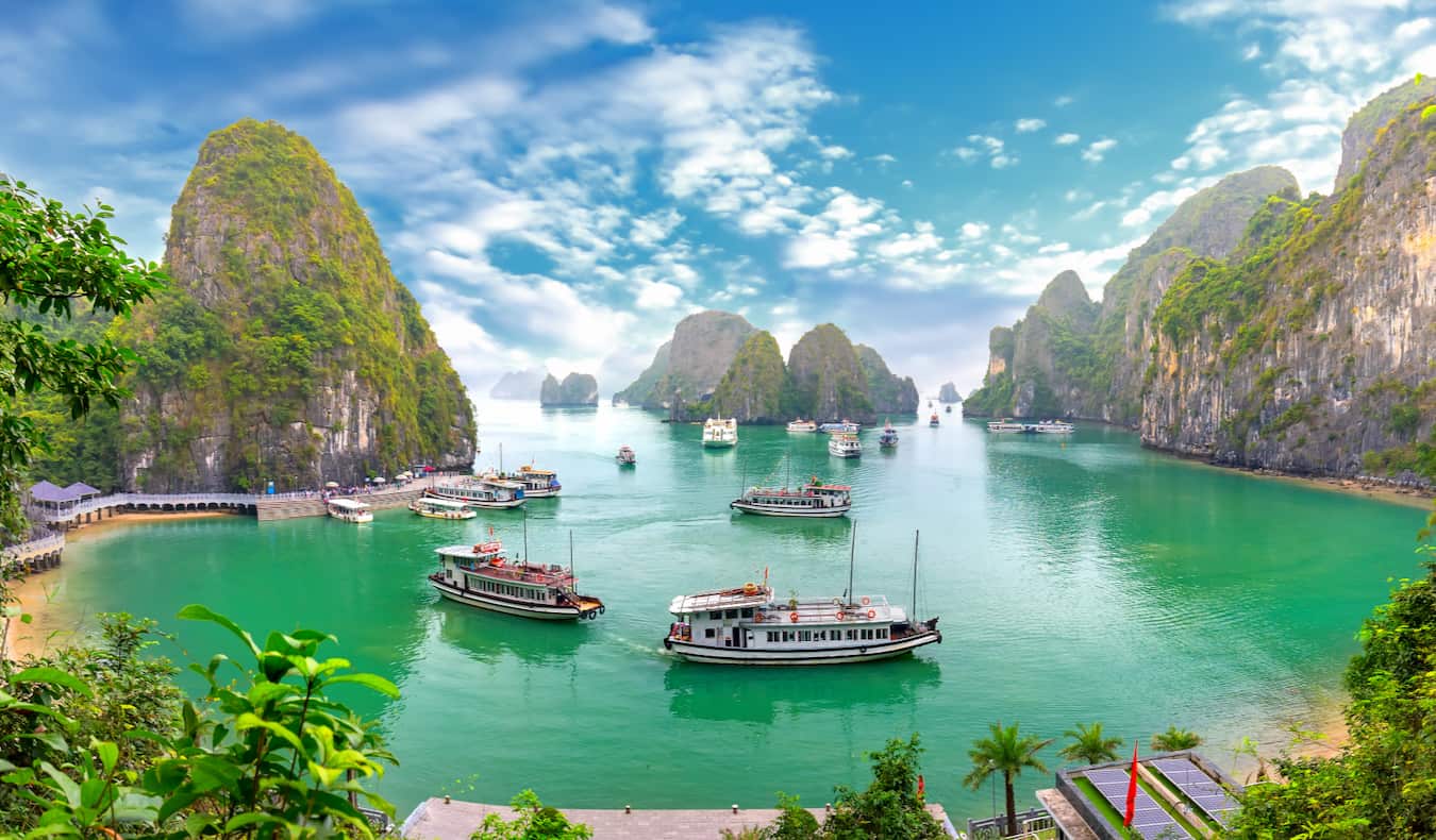 Boats in the calm waters of Ha Long Bay near Hanoi, Vietnam surrounded by tall mountains