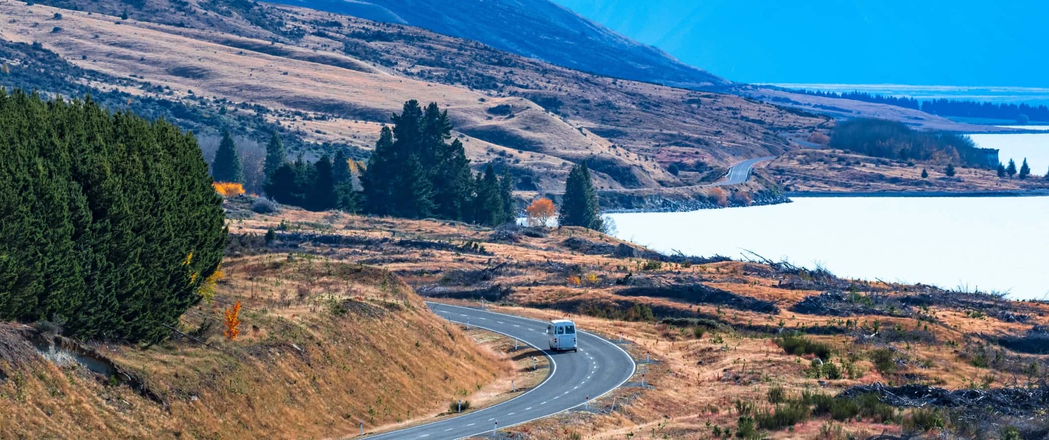 Van driving down a winding road along a lake near Wanaka, New Zealand