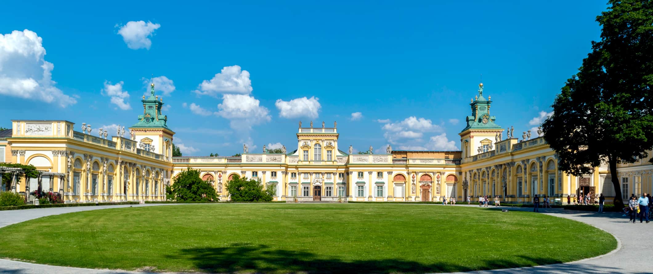 A wide, regal palace surrounding by green grass on a sunny day in Warsaw, Poland