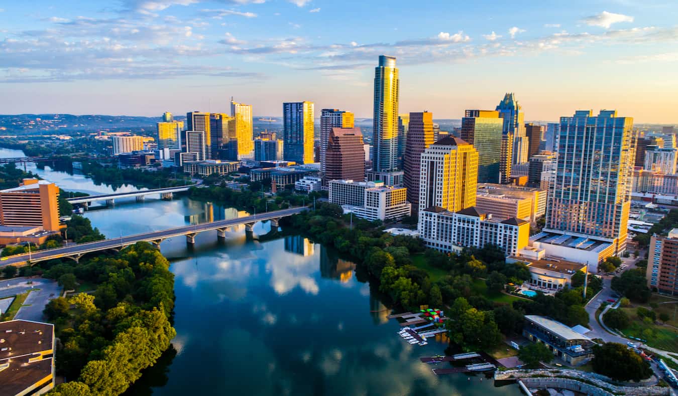 An aerial view of downtown Austin, Texas during golden hour, featuring tall skyscrapers along the water