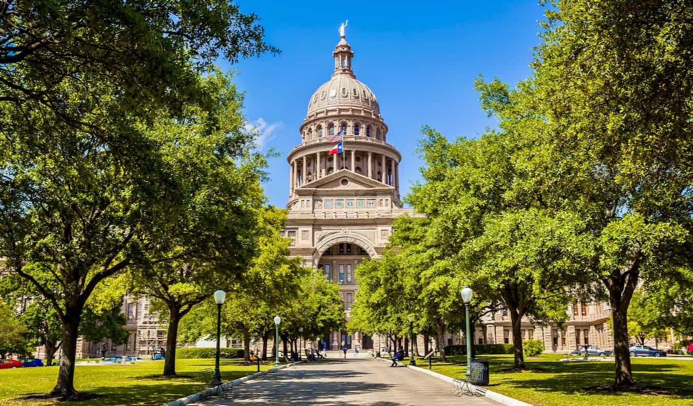 The State Capitol Building surrounded by trees and greenery in Austin, Texas.