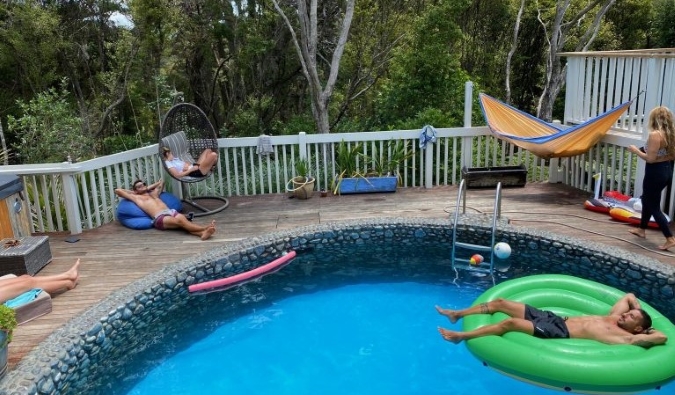 People lounging in and around an outdoor pool at Hekerua Lodge Backpackers hostel on Waiheke Island in New Zealand