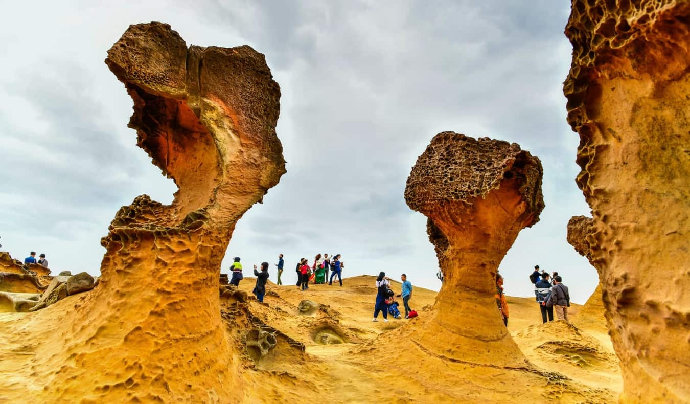 People walking around huge, sandstone colored rock formations in Yehliu Geopark, Taiwan