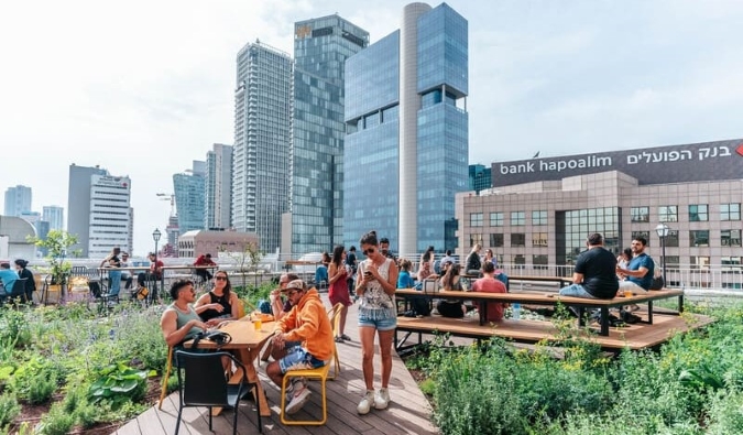 People hanging out on the rooftop hostel of Abraham Tel Aviv hostel, with skyscrapers in the background, in Tel Aviv, Israel