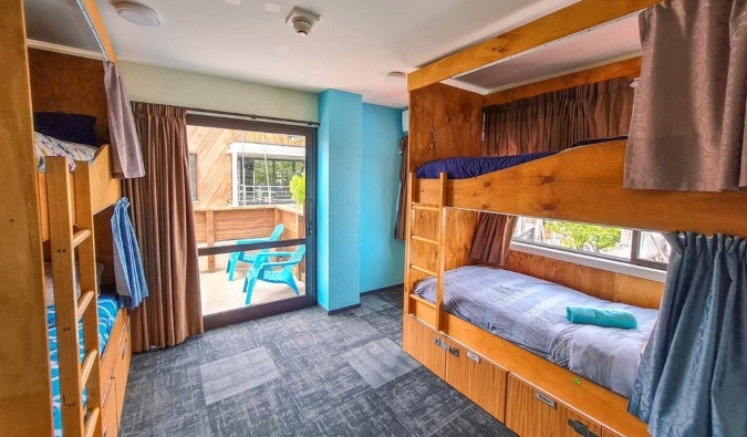 Wooden bunk beds with curtains in a bright room at Adventure Queenstown Hostel in Queenstown, New Zealand.