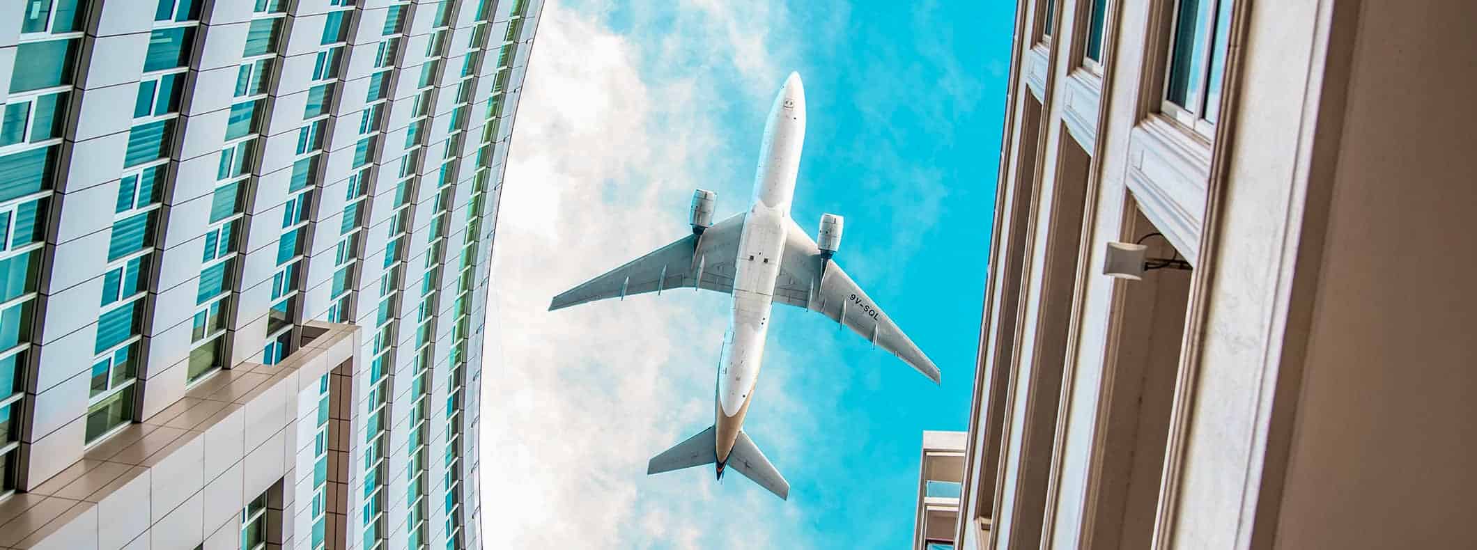 A commercial airplane flying over a city, as seen from the ground looking up between buildings