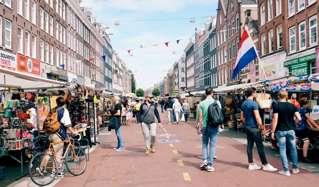 People walking down a narrow, busy street in sunny Amsterdam as the browse little shops