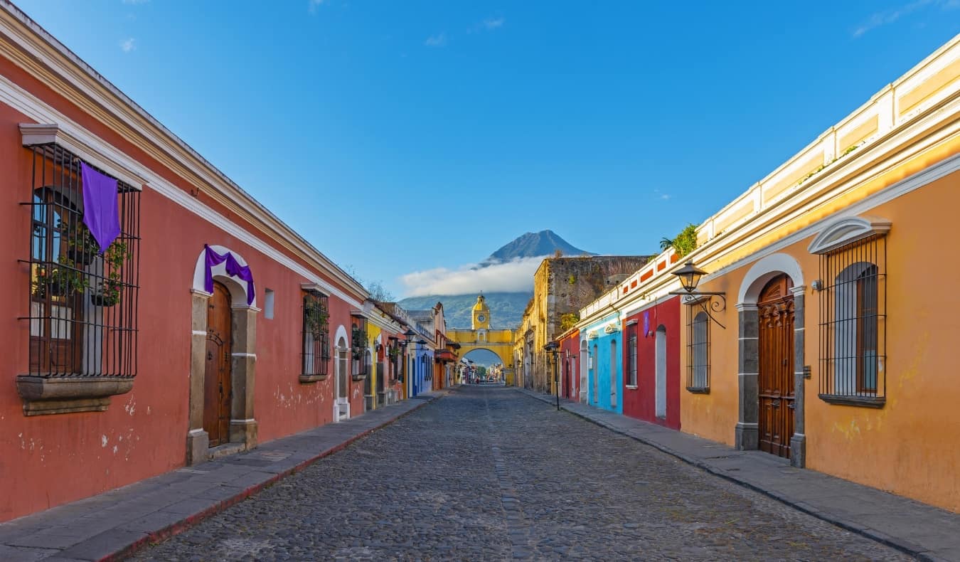 Cityscape of Antigua, Guatemala with brightly colored houses and a mountain rising through the clouds in the background