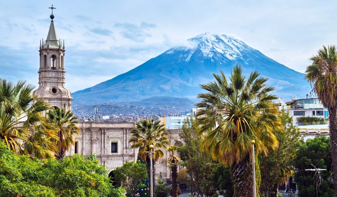 Skyline of Arequipa in Peru, with a historic church and palm trees in the foreground and a volcano in the background